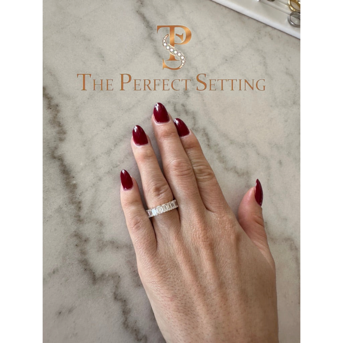 The Perfect Setting, Inc. emerald-cut diamond eternity band worn on a finger with dark red nail polish.