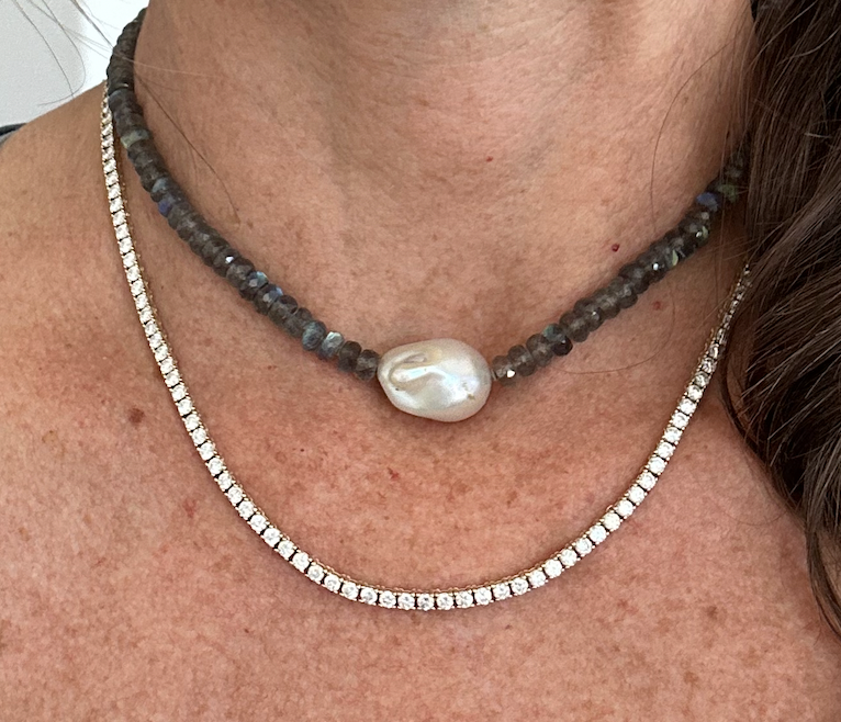 Close-up of a person wearing diamond tennis necklaces with a pearl pendant.