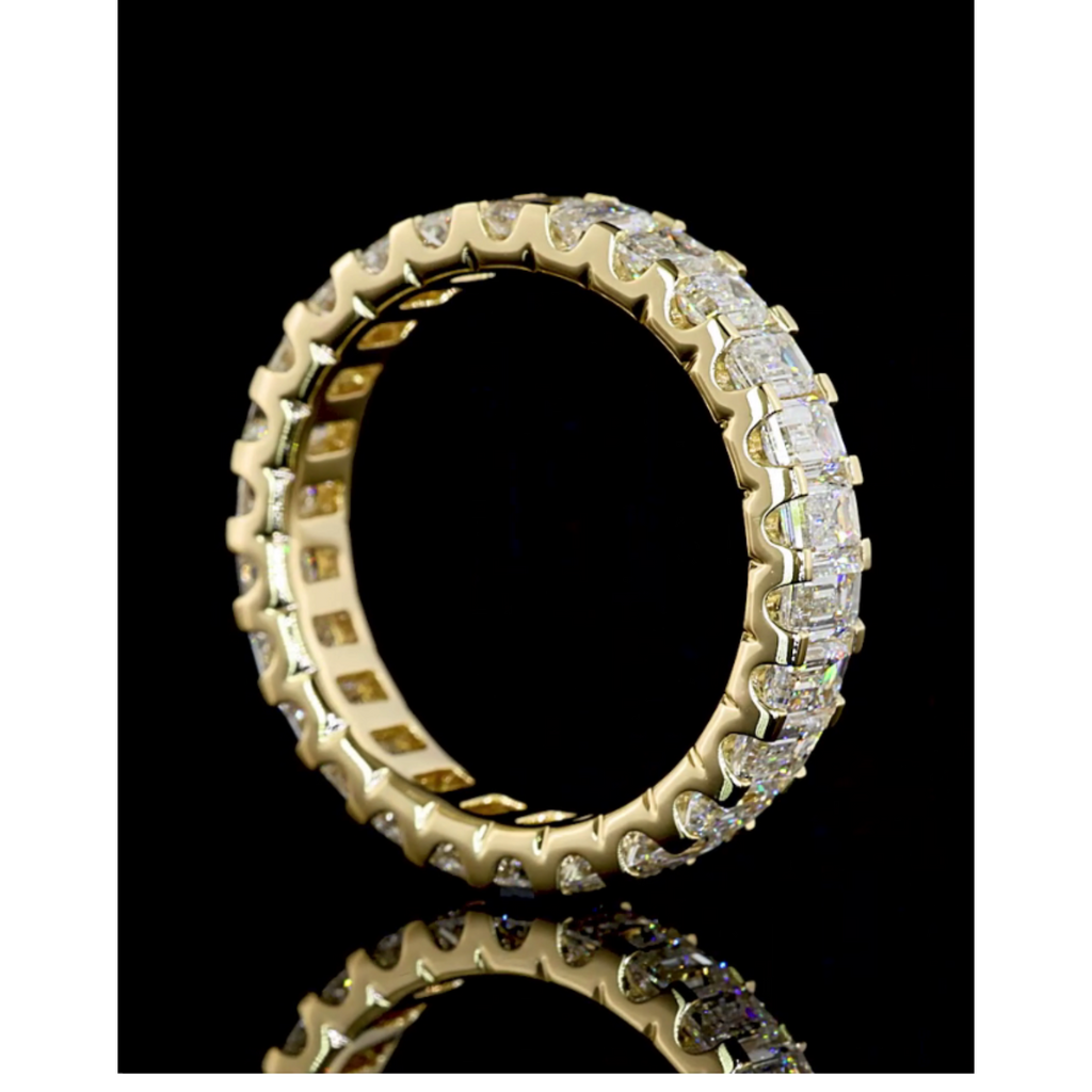 The Perfect Setting, Inc. custom emerald-cut diamond eternity band in yellow gold on a black reflective surface.