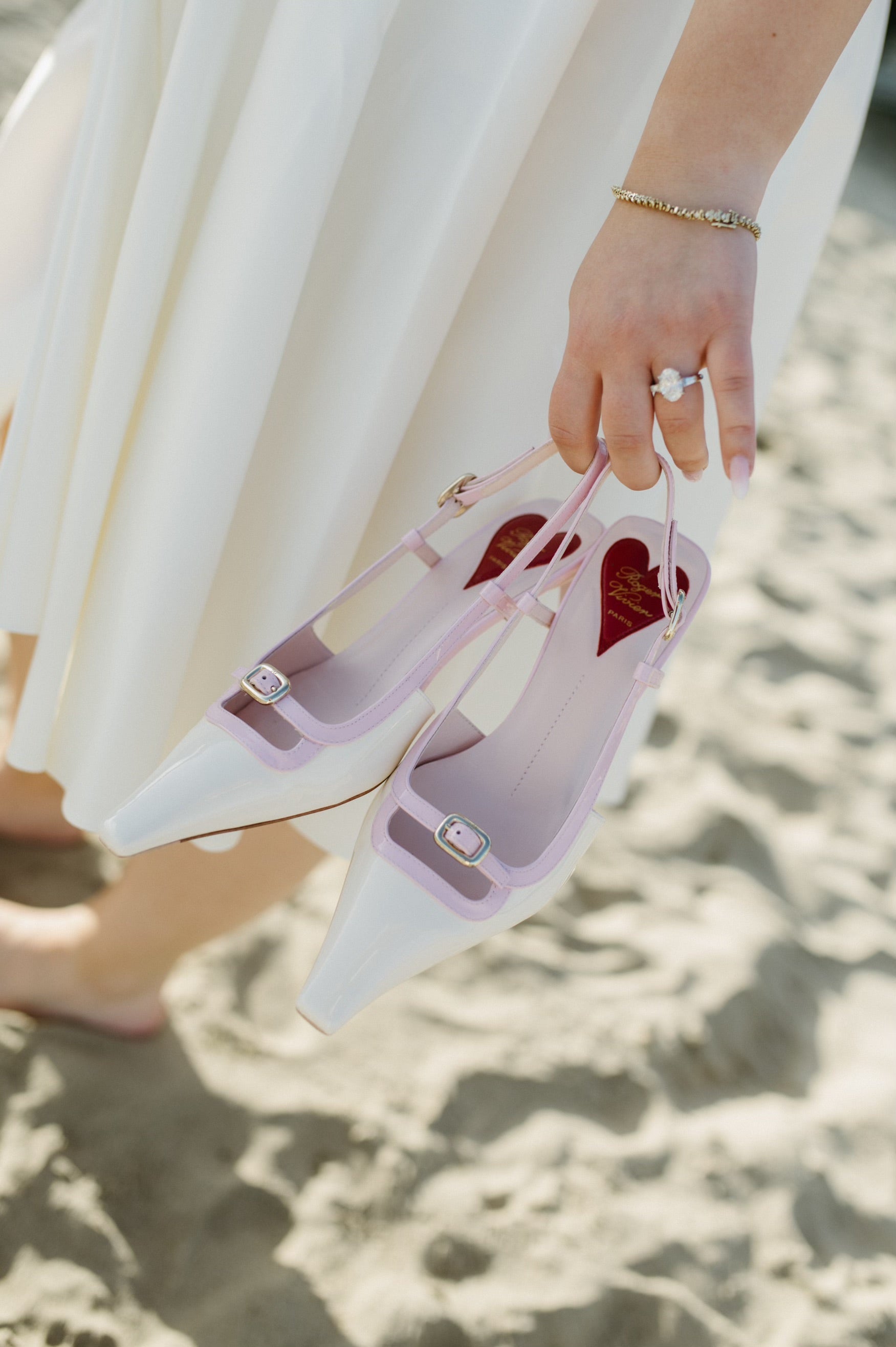 The Perfect Setting, Inc. oval diamond engagement ring with tapered baguettes worn on a hand holding pink slingback shoes