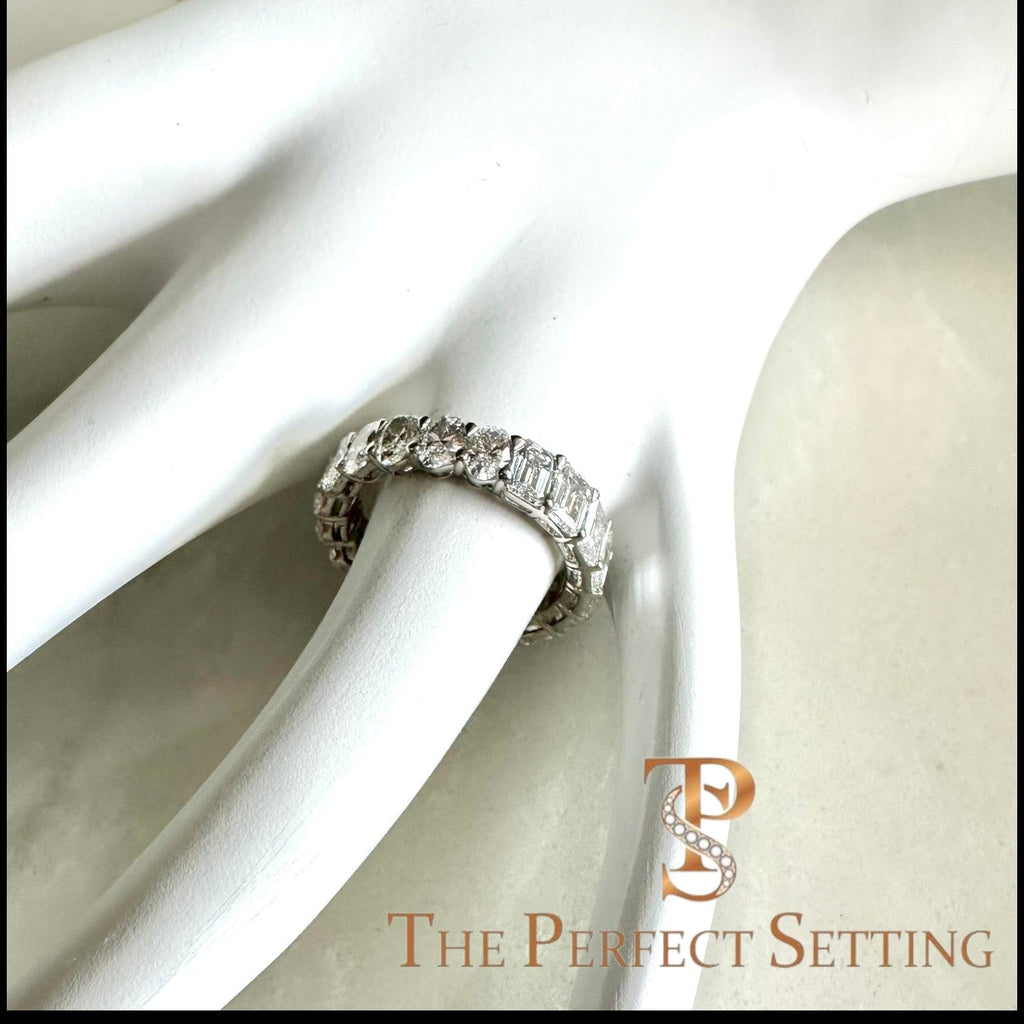 The Perfect Setting, Inc. platinum eternity band featuring alternating emerald and oval cut diamonds on a white display.