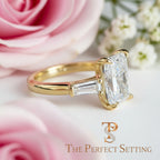 A yellow gold ring featuring a large rectangular radiant cut diamond in a prong setting with smaller baguette side stones, shown on a light neutral background with the 'The Perfect Setting' logo at the bottom.