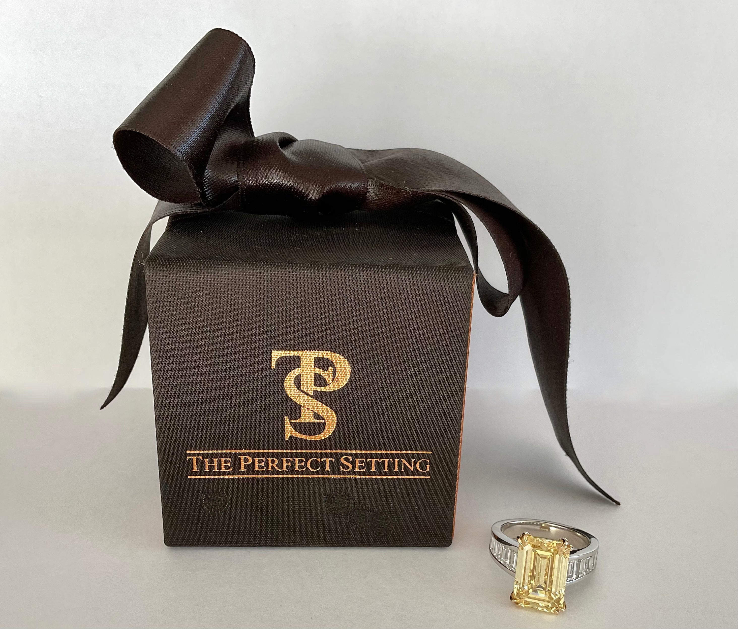 The Perfect Setting, Inc emerald cut vivid yellow diamond engagement ring with baguette side stones next to a gift box